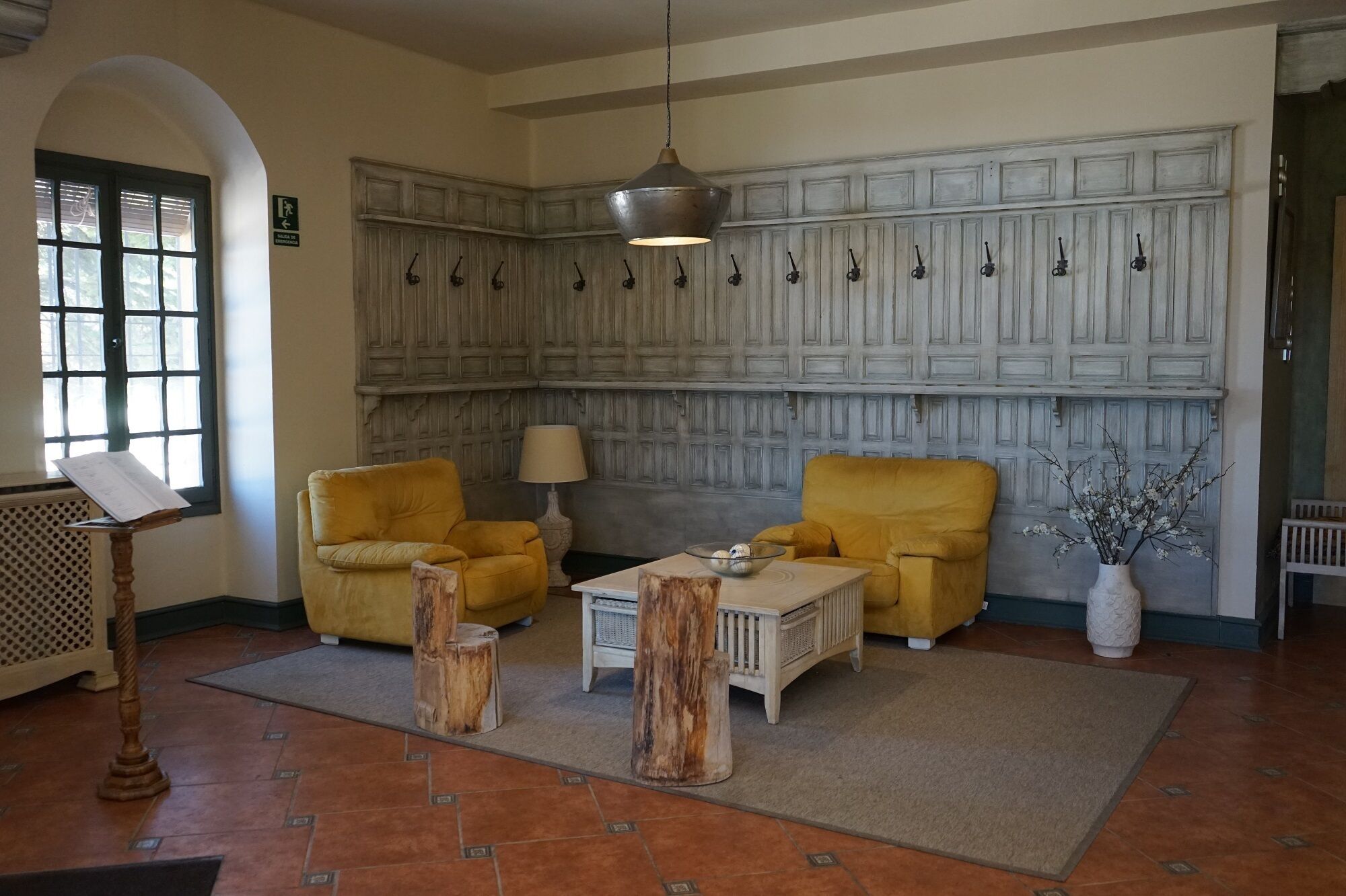 A room with two yellow armchairs, a white coffee table, a lamp, and a wall with multiple hooks.