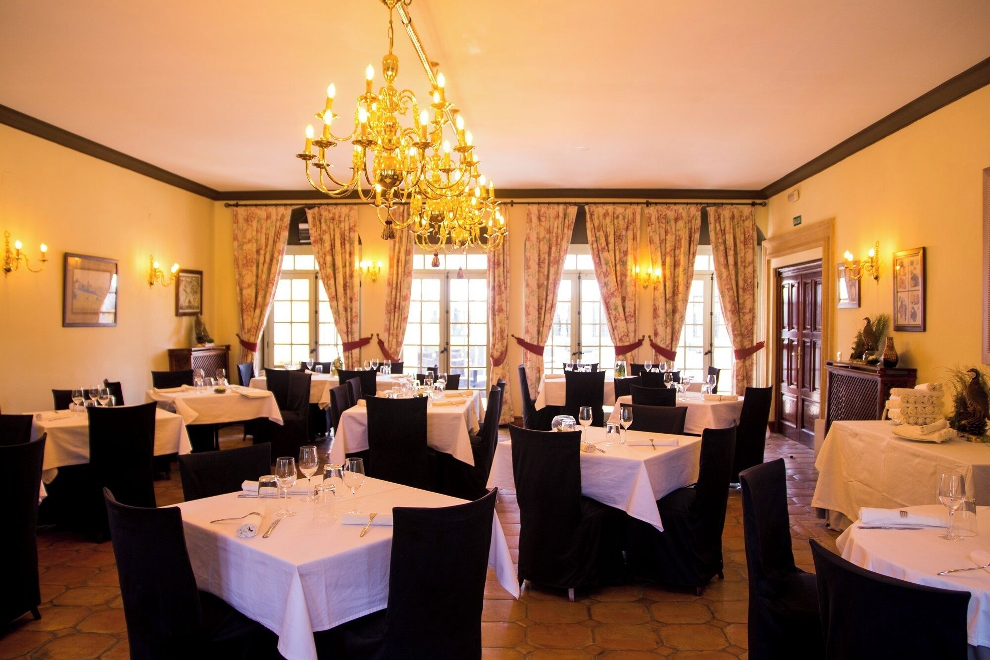 Un restaurante con varias mesas, sillas negras y un candelabro.