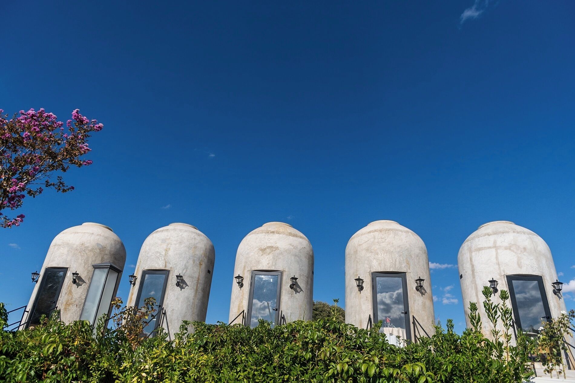 A row of five cylindrical structures with windows and doors, surrounded by greenery.