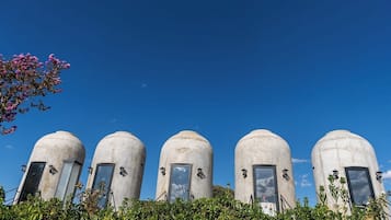 A row of five cylindrical structures with windows and doors, surrounded by greenery.