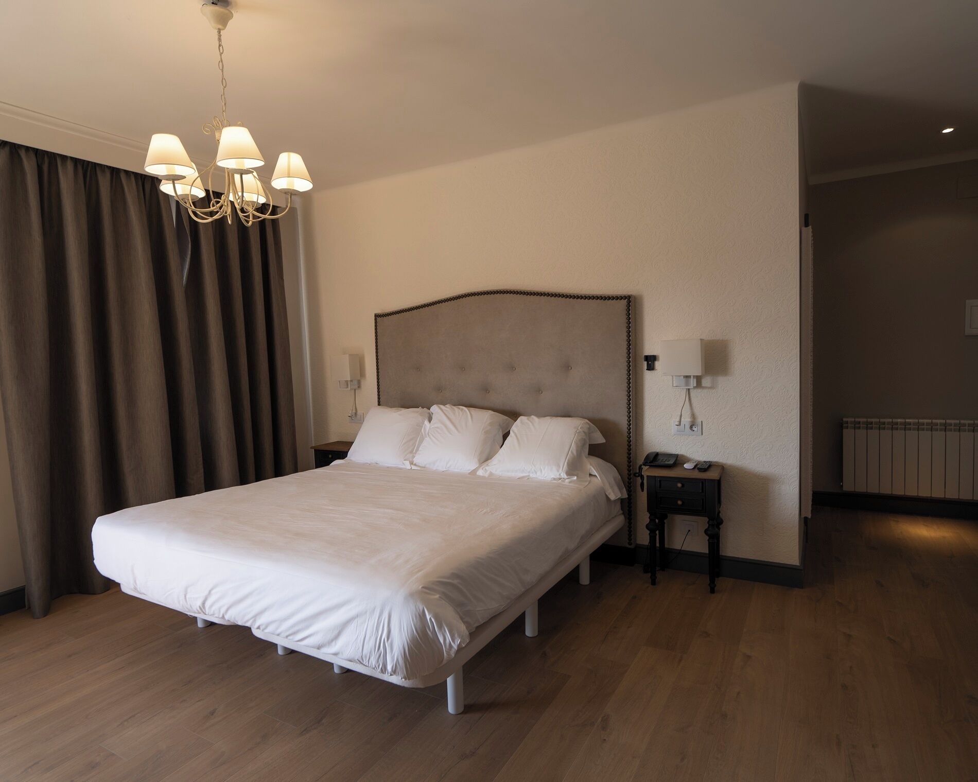 Habitación de hotel con una cama grande, un candelabro, una mesita de noche con lámpara y un radiador.