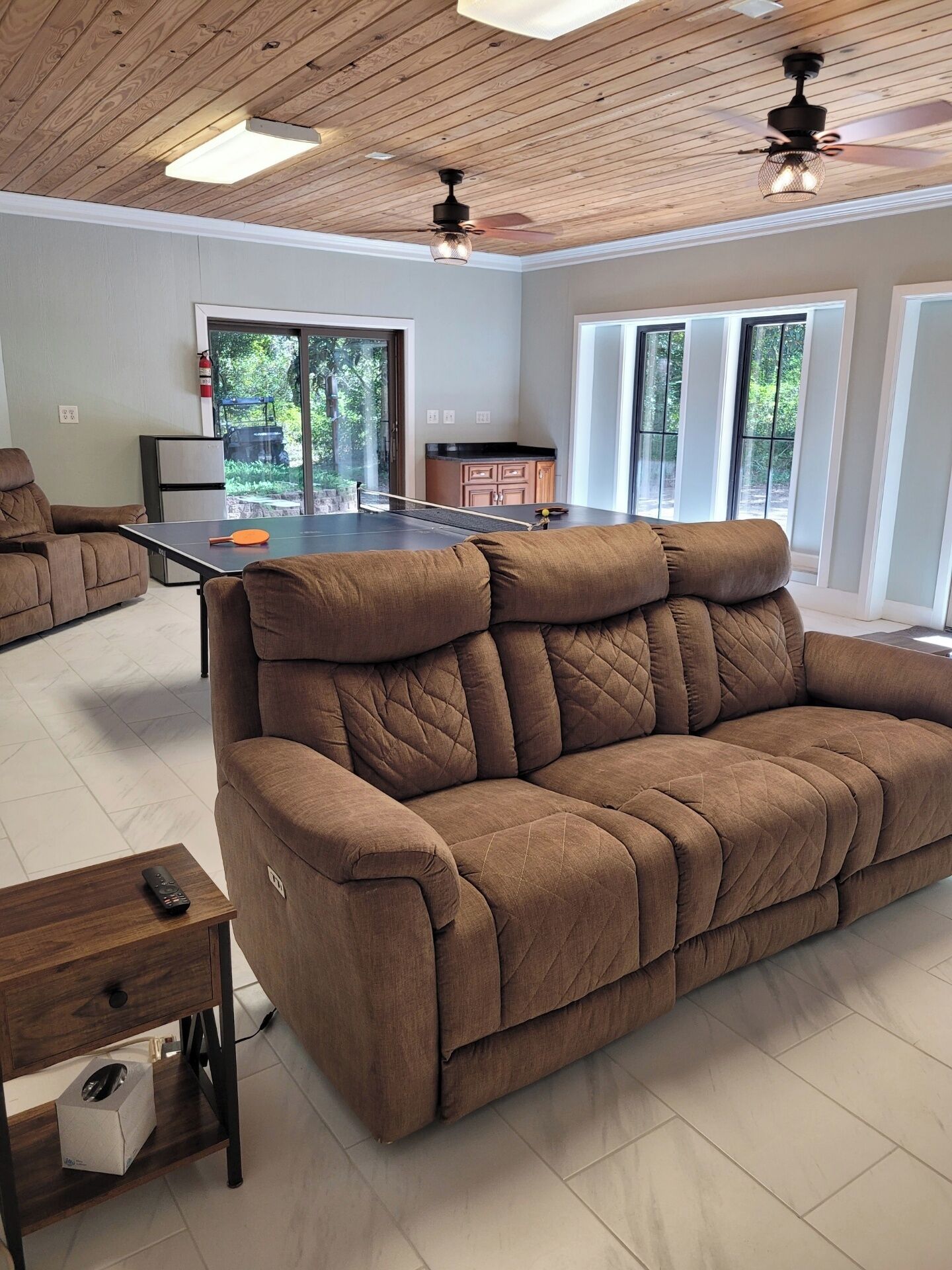 Ein Wohnzimmer mit braunem Sofa, einem Tischtennis-Tisch und einem Deckenventilator.