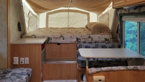 Een compact camperinterieur met een bed, een kleine kitchenette en een raam met uitzicht op groen.