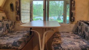 Een compact RV-interieur met een eethoek, twee comfortabele zitplaatsen, een raam met uitzicht op groen, en houten kastjes.