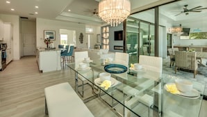 Un espace repas moderne avec une table en verre, des chaises blanches et un lustre.