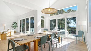 A spacious dining area with a wooden table set for six, surrounded by chairs, large windows, and a view of the outdoors. - 9 Juniper @ Forest Beach | Oceanfront | Pool & Spa | 6 King Suites (Hilton Head Island)