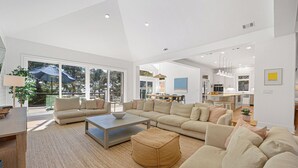 A spacious living area with a large sectional sofa, a coffee table, and a dining area with a kitchen in the background. - 9 Juniper @ Forest Beach | Oceanfront | Pool & Spa | 6 King Suites (Hilton Head Island)