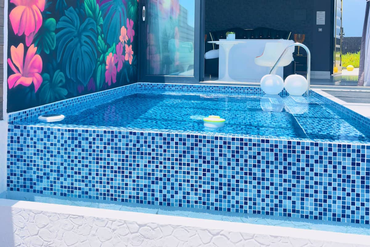 A modern indoor swimming pool with a vibrant mural, a jacuzzi, and a clear view of the outdoors.