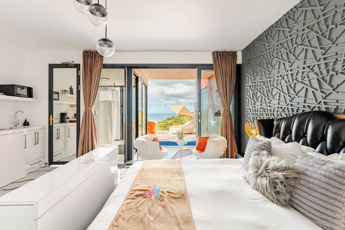 A modern hotel room with a bed, a desk, a bathroom, and a balcony with a pool view.