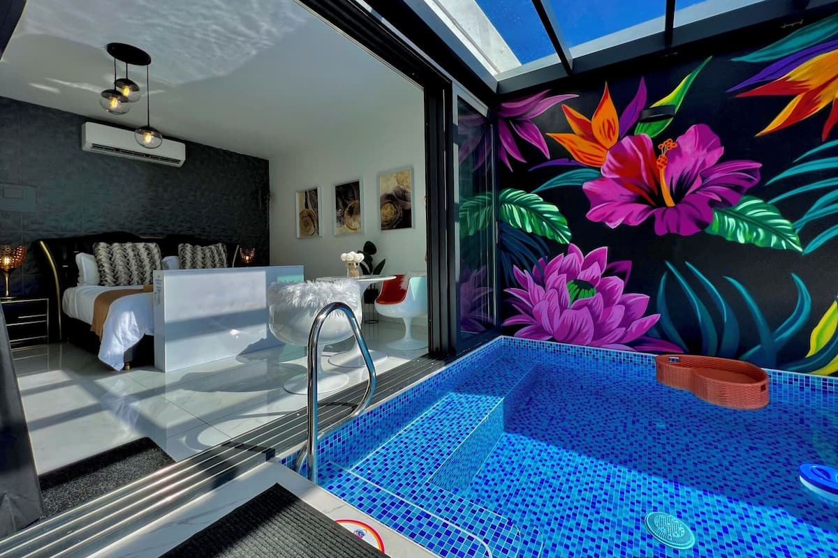 A modern bathroom with a glass-enclosed jacuzzi, a white vanity, and a vibrant floral mural on the wall.
