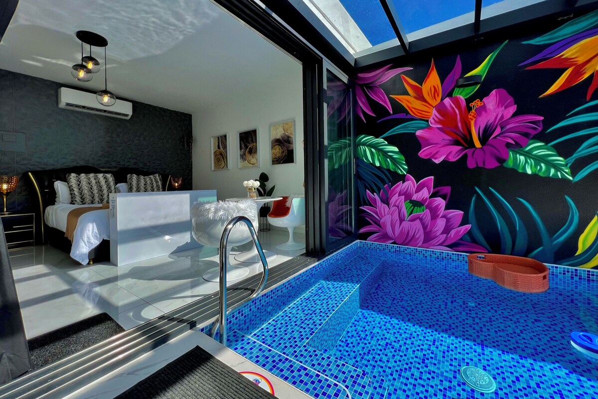 Un baño moderno con un jacuzzi de vidrio, un tocador blanco y un vibrante mural floral en la pared.