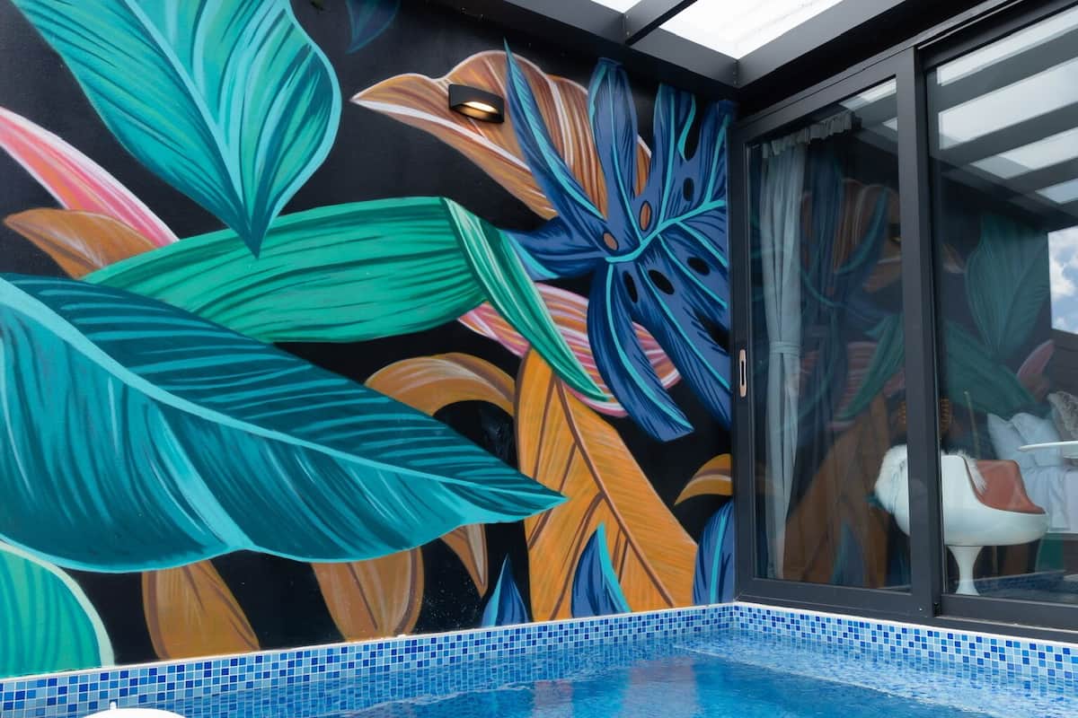 A pool area with a tiled floor, a glass enclosure, and a colorful mural with large leaves.