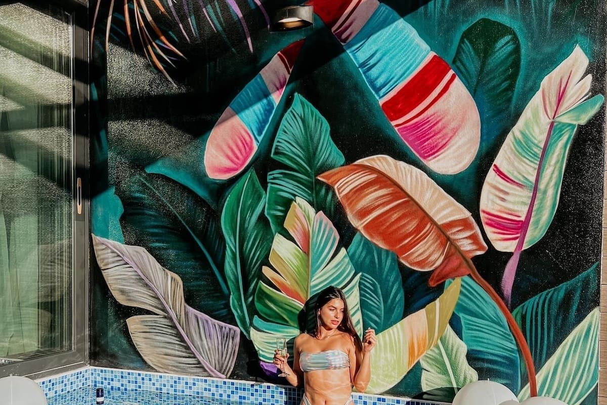 A person in a swimming pool with a tropical mural in the background.
