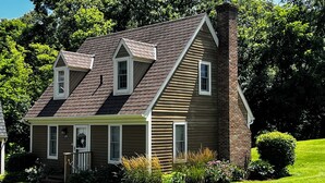 A two-story house with a gabled roof, a brick chimney, and a front porch.