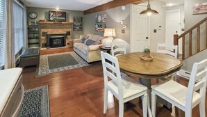 A cozy living room with a fireplace, a dining table with chairs, and a staircase leading to another level.