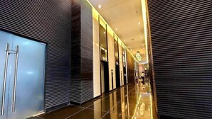 A modern hotel corridor with reflective flooring, a metallic elevator, and a patterned wall. - 1 Bedroom with Balcony Condo Apartment in Makati City (Makati)