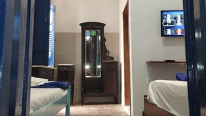 A hotel room with a wooden floor, a bed with a white mattress, a wooden wardrobe, a small table with a lamp, and a television mounted on the wall. - Pousada e Hostel Andarai (Andaraí)