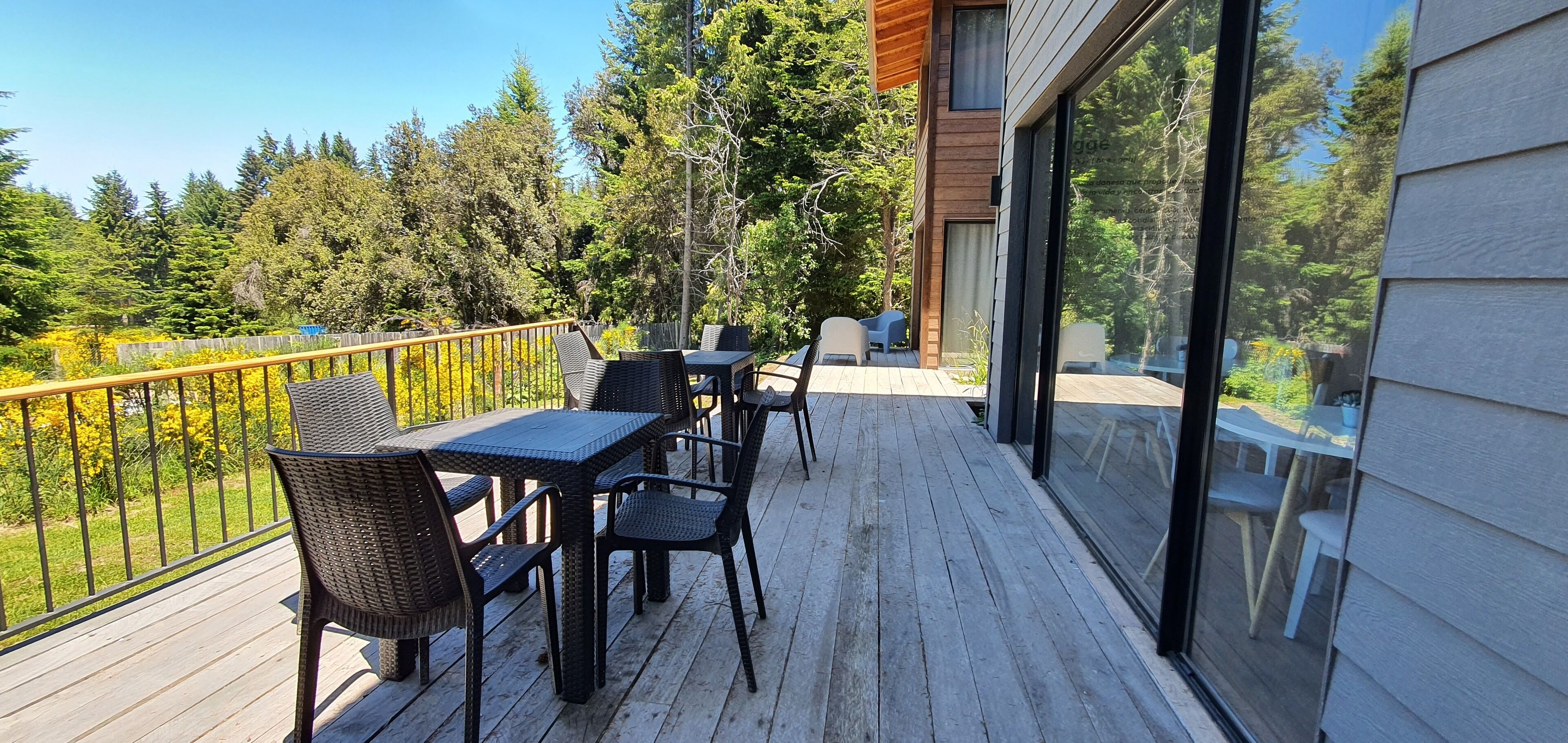 A wooden deck with outdoor furniture, a glass railing, and a view of a forested area.