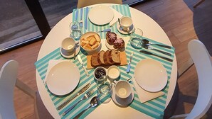 A round table with a striped tablecloth, plates, cutlery, and a bowl of muffins. - Hygge Haus (Villa La Angostura)