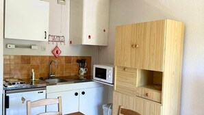 A compact kitchen with white cabinets, a microwave, a sink, and a wooden dining table with chairs. - Studio le Coquelicot (L ESPEROU)
