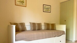 A single-bed room with a white bed, striped pillows, and two framed pictures on the wall. - Studio le Coquelicot (L ESPEROU)