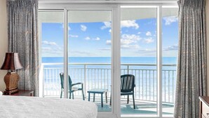 A bedroom with a large sliding glass door leading to a balcony with a view of the ocean. - Unforgettable Getaway 3BR (Myrtle Beach)