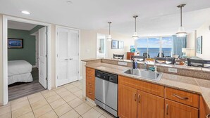 A modern kitchen with a dishwasher, wooden cabinets, and a large window overlooking the sea. - Unforgettable Getaway 3BR (Myrtle Beach)