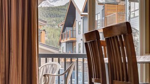 A view from a balcony with wooden chairs, overlooking a mountain and buildings with balconies.