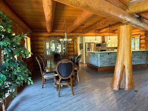 A rustic log cabin interior with a dining area, a kitchen, and a large wooden tree trunk pillar. - Opulent Oaks Chalet
 (Agassiz)