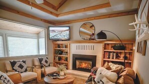 A cozy living room with a leather sofa, a fireplace, a television, and a ceiling fan. - Hot tub, fire pit, 6 min to beach & ski, sleeps 6 (Stateline)