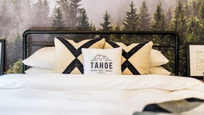 A bed with a black metal frame, white bedding, and pillows with a black and white pattern. A pillow has text and a mountain graphic. - Hot tub, fire pit, 6 min to beach & ski, sleeps 6 (Stateline)