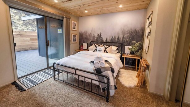 A bedroom with a bed, a nightstand, a wall mural, and a sliding glass door leading to an outdoor deck. - Hot tub, fire pit, 6 min to beach & ski, sleeps 6 (Stateline)
