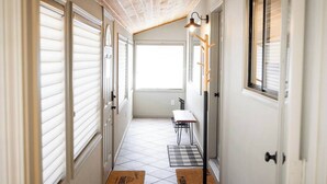 A narrow hallway with white walls, a sloped ceiling, and a window at the end. There are two doors on the left, a bench, and a wall-mounted light fixture. - Hot tub, fire pit, 6 min to beach & ski, sleeps 6 (Stateline)