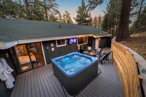 Un bain à remous sur une terrasse en bois, avec vue sur une montagne et des arbres.