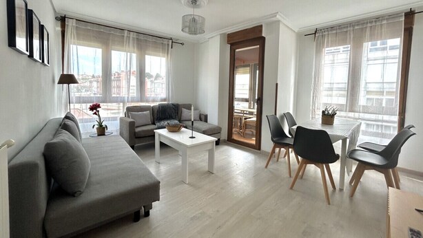 A modern living room with a grey sofa, a white coffee table, and a dining area with black chairs and a white table.