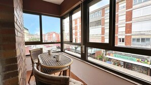 A balcony with wicker furniture, large windows, and a view of buildings and a street.
