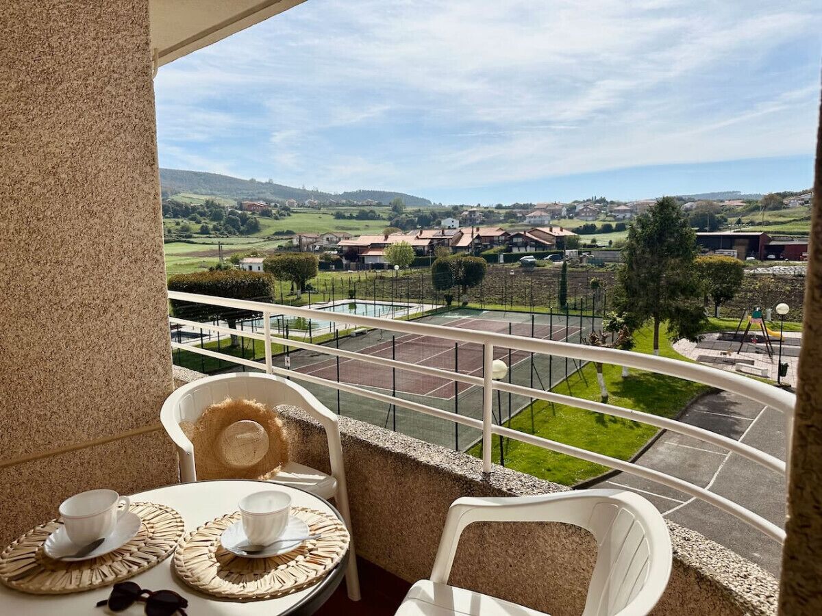 Un balcón con una mesa dispuesta para dos personas, con vistas a una cancha de tenis y un paisaje verde.