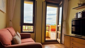 Ett mysigt vardagsrum med en röd soffa, en tv och en skjutdörr i glas som leder ut till en balkong med utsikt över himlen och ett avlägset landskap.