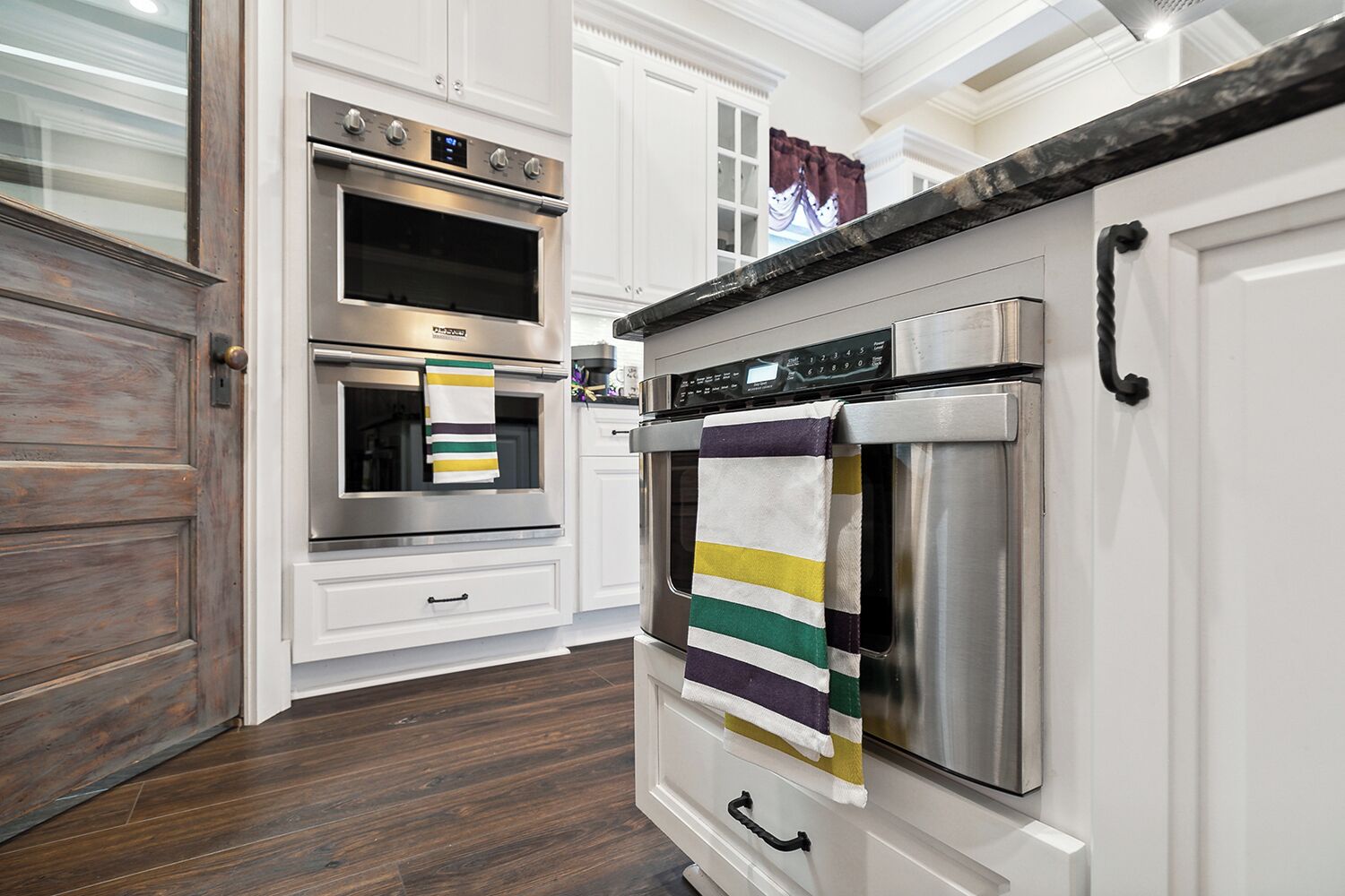 A modern kitchen with white cabinetry, stainless steel appliances, and a wooden floor.