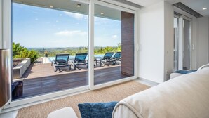 Ein modernes Wohnzimmer mit einem großen Schiebeglastür, die auf eine Terrasse mit Liegestühlen und einem Pool führt.