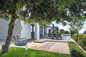A modern outdoor patio with a hammock, lounge chairs, and a swimming pool. - Luxury Private Villa | Casa da Colina (Caldas de Monchique)