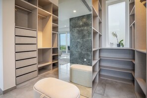 A modern closet with multiple shelves and a bench, a marble accent wall, and a view of the outdoors. - Luxury Private Villa | Casa da Colina (Caldas de Monchique)