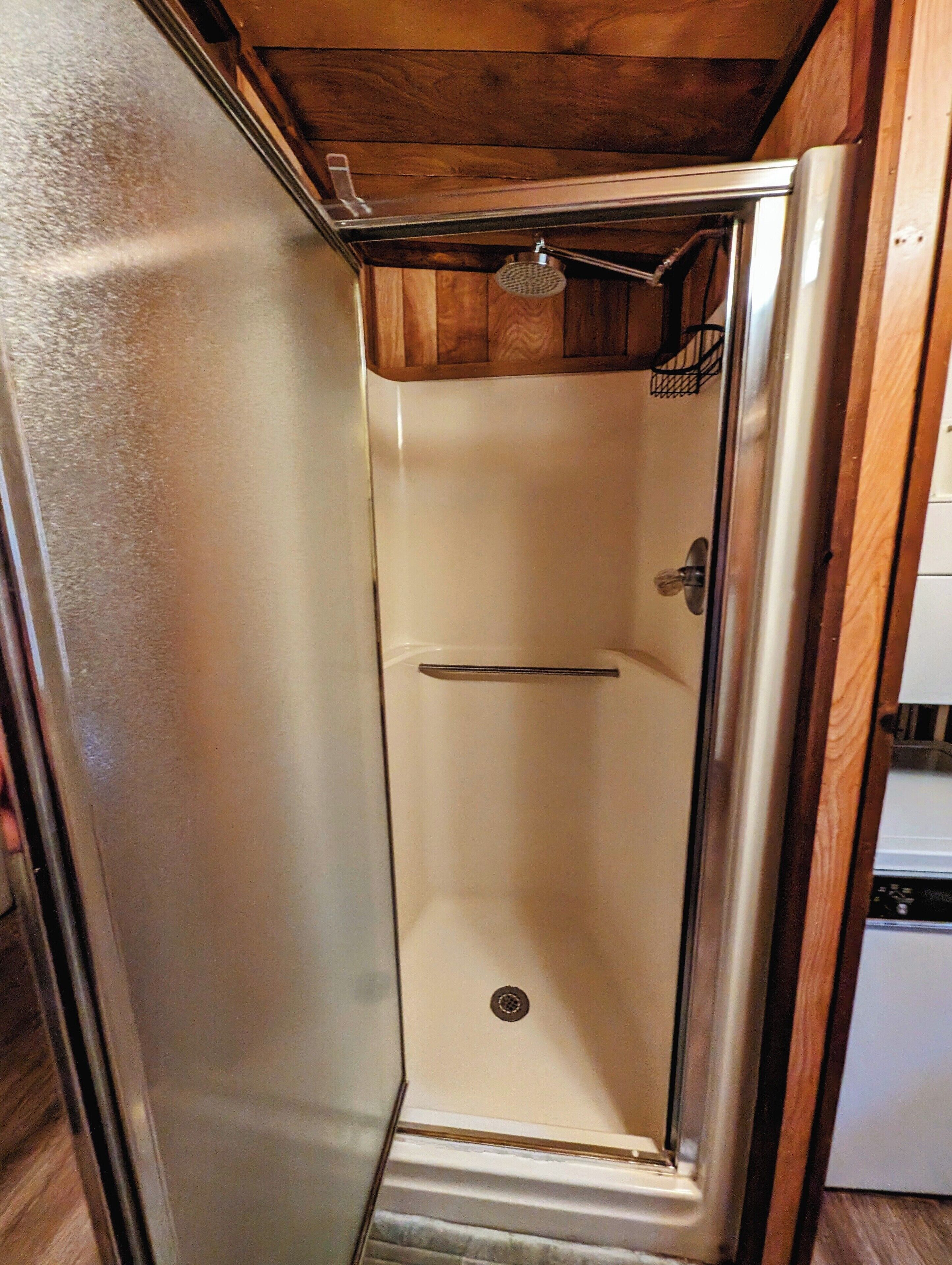Un espacio de ducha compacto y cerrado, con techo de madera y puerta metálica.