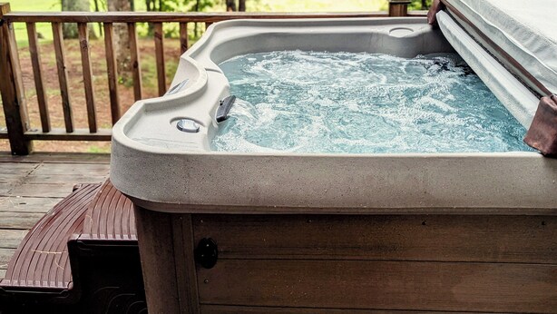 Un bain à remous sur une terrasse en bois, avec vue sur une zone boisée.