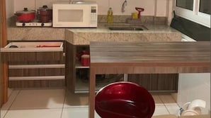 A compact kitchen with a microwave, stove, and sink. There is a window to the right and a cabinet above the sink. - Israel Tambaú - APTO Luxuoso Beira Mar  (João Pessoa)