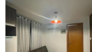 A room with a sofa, a door, and a ceiling light fixture. - Israel Tambaú - APTO Luxuoso Beira Mar  (João Pessoa)