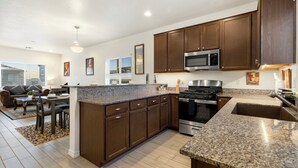 A modern kitchen with dark wooden cabinets, granite countertops, stainless steel appliances, and a dining area with a sofa and table.