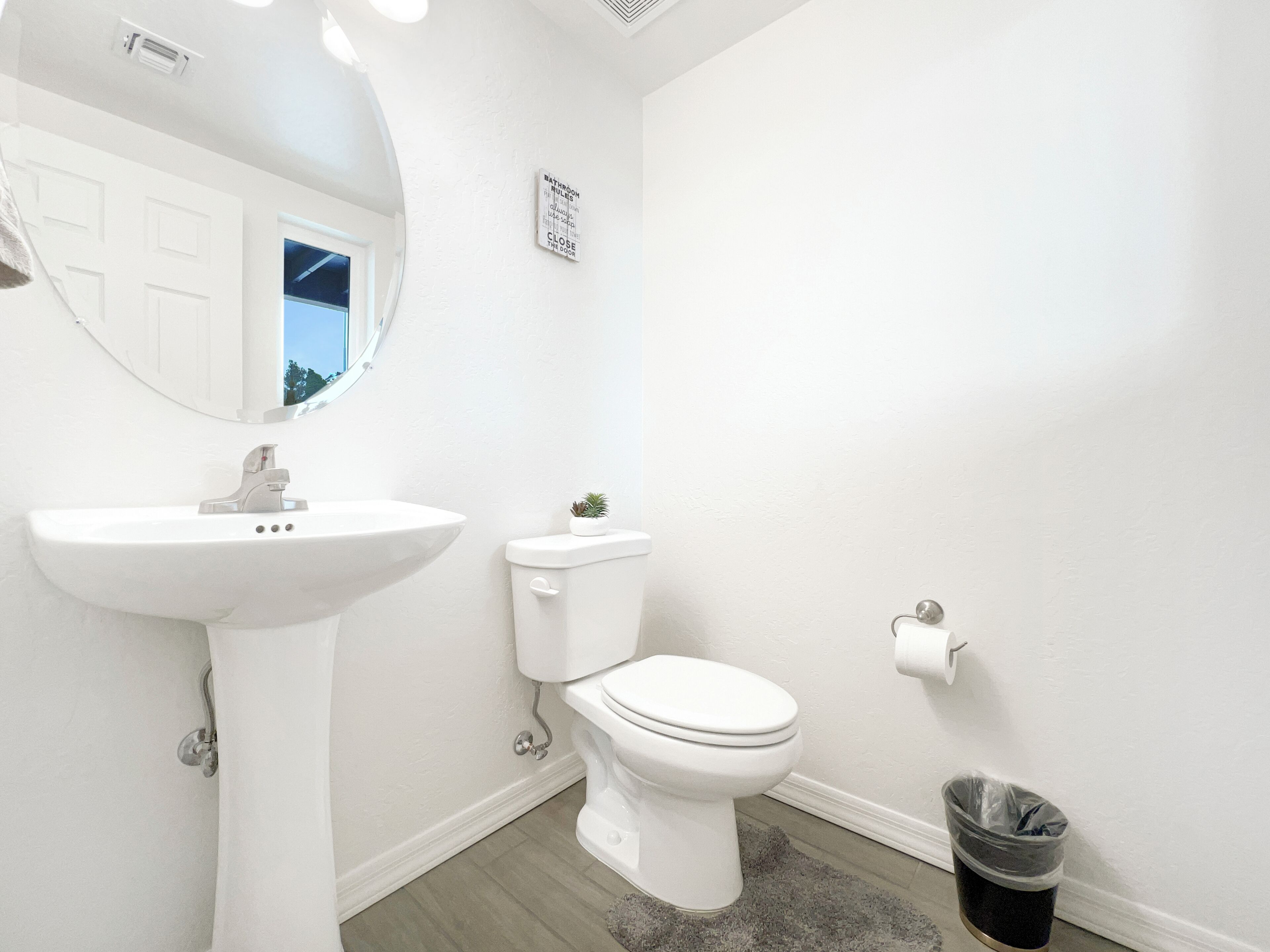 A bathroom with a white sink, toilet, and a small trash bin.