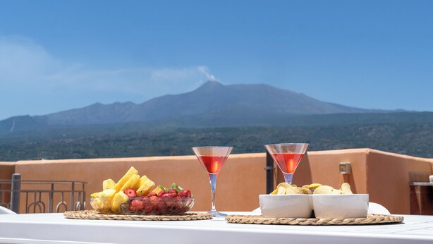 A table with fruit and snacks, two martini glasses, and a view of a mountain. - Terrazza sul Mare - Appartamento (Mascali)
