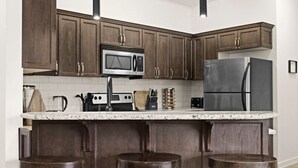 Una cocina con armarios de madera oscura, un refrigerador de acero inoxidable, un microondas y una encimera de granito.